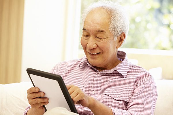 A senior male enjoying listening to sound with an assistive listening device while using a tablet pc