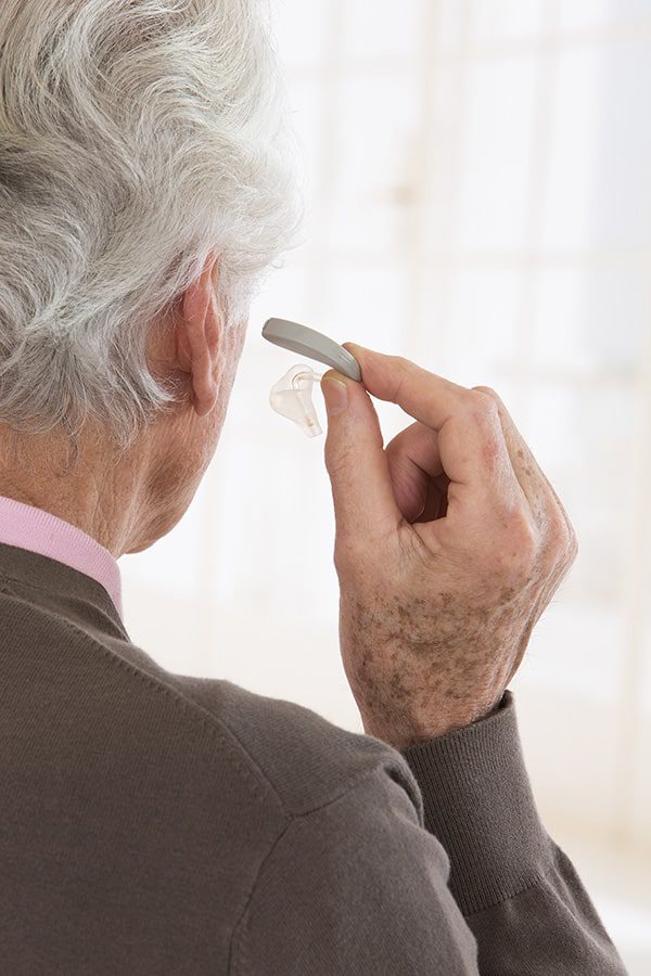 A senior male hold a prescription hearing aid near his ears