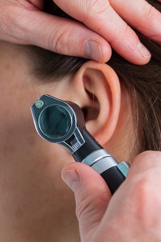 Doctor of audiology inspecting a girl's ear using an otoscope
