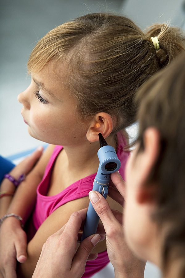 Hearing professional inspecting a girl's ear using a otoscope